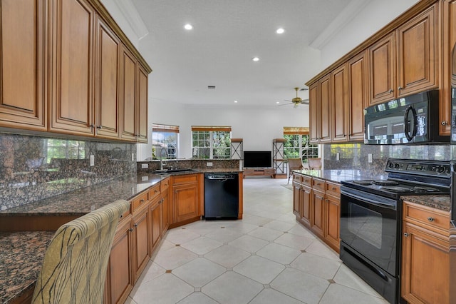 kitchen featuring ornamental molding, brown cabinetry, a sink, dark stone counters, and black appliances