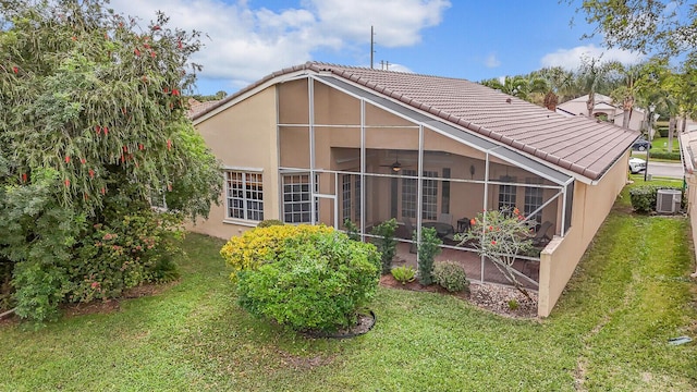 back of property with glass enclosure, a tile roof, ceiling fan, a yard, and central air condition unit