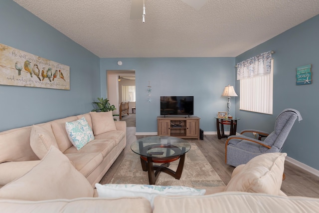 living room featuring ceiling fan, a textured ceiling, and light wood-type flooring