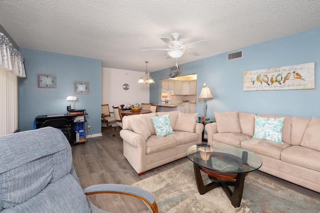 living room with hardwood / wood-style floors, ceiling fan with notable chandelier, and a textured ceiling