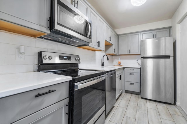 kitchen featuring stainless steel appliances, gray cabinets, sink, and decorative backsplash