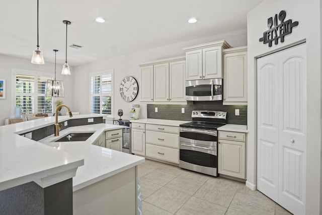 kitchen featuring sink, stainless steel appliances, cream cabinets, decorative backsplash, and decorative light fixtures