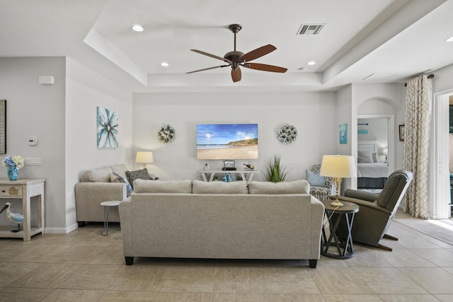 living room with a raised ceiling and ceiling fan