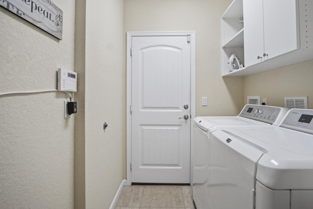 clothes washing area with cabinets, washer and dryer, and light hardwood / wood-style flooring