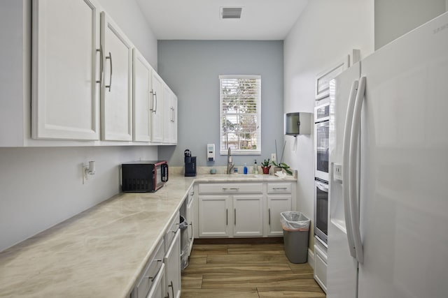 kitchen with sink, white cabinetry, stainless steel oven, white fridge with ice dispenser, and hardwood / wood-style floors