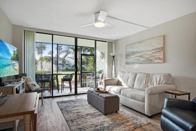 living area featuring a ceiling fan, a wall of windows, and wood finished floors