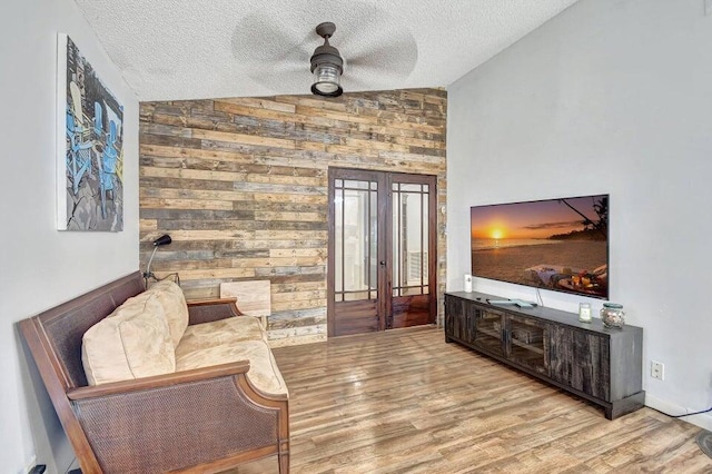 living area with a textured ceiling, french doors, ceiling fan, wood finished floors, and vaulted ceiling