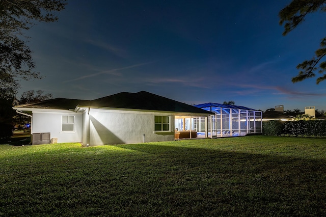 back house at dusk featuring a lanai and a lawn