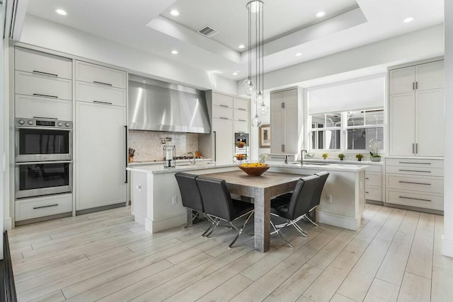 kitchen featuring pendant lighting, a kitchen breakfast bar, a raised ceiling, and a kitchen island with sink