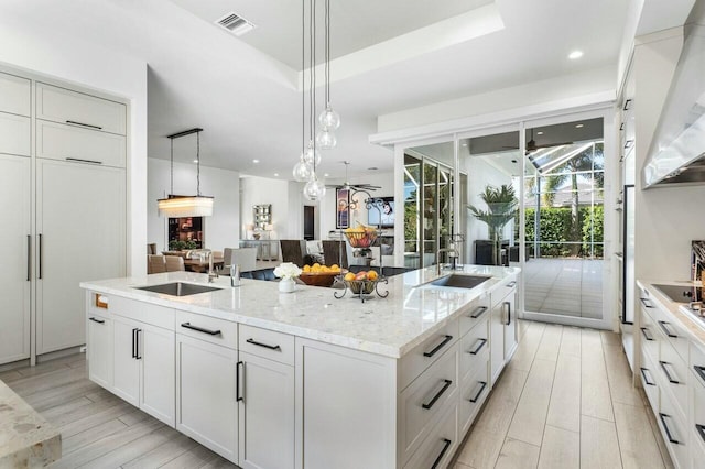 kitchen featuring sink, white cabinetry, light stone counters, pendant lighting, and a kitchen island with sink