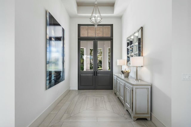 foyer featuring a high ceiling, a tray ceiling, a notable chandelier, and french doors