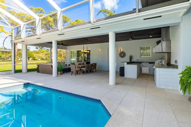 view of pool with ceiling fan, glass enclosure, a patio area, an outdoor hangout area, and exterior kitchen