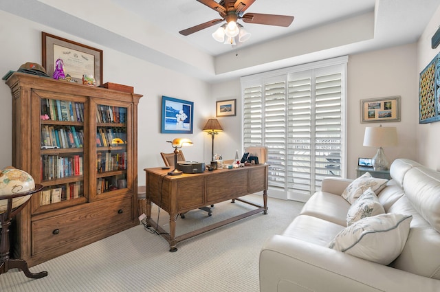 office space featuring light colored carpet, ceiling fan, and a tray ceiling