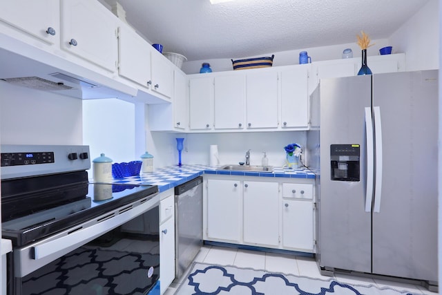 kitchen with sink, tile countertops, light tile patterned floors, appliances with stainless steel finishes, and white cabinets