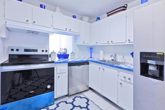 kitchen with appliances with stainless steel finishes, sink, tile counters, and white cabinets