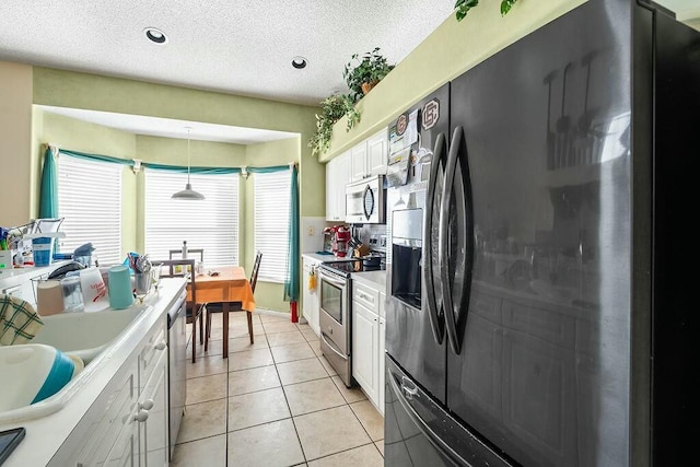 kitchen featuring white cabinetry, a textured ceiling, hanging light fixtures, light tile patterned floors, and stainless steel appliances