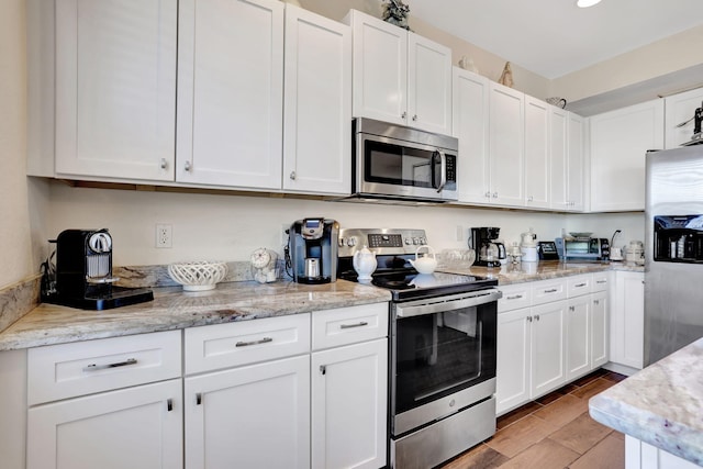 kitchen with white cabinetry, stainless steel appliances, and light stone countertops