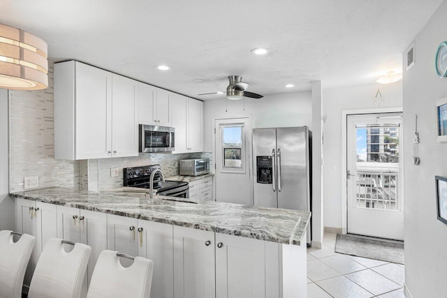 kitchen with appliances with stainless steel finishes, light stone counters, white cabinets, decorative backsplash, and kitchen peninsula