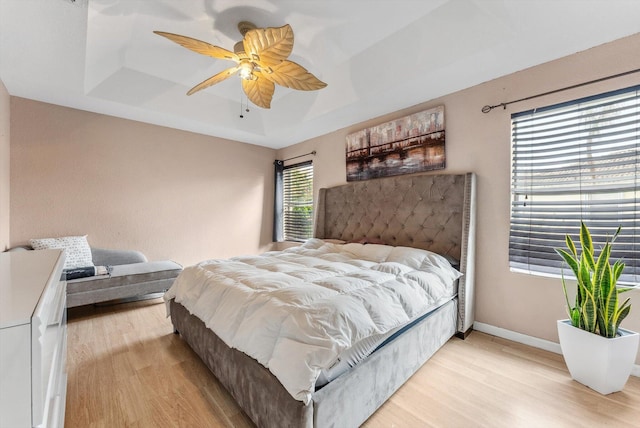 bedroom with ceiling fan, light hardwood / wood-style floors, and a raised ceiling