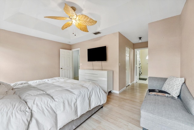 bedroom with ceiling fan, light hardwood / wood-style flooring, and a raised ceiling