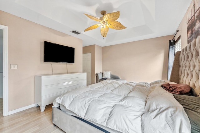 bedroom with light wood-type flooring, a tray ceiling, and ceiling fan