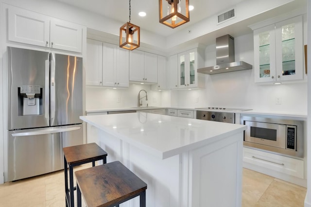 kitchen featuring pendant lighting, wall chimney range hood, sink, appliances with stainless steel finishes, and a center island