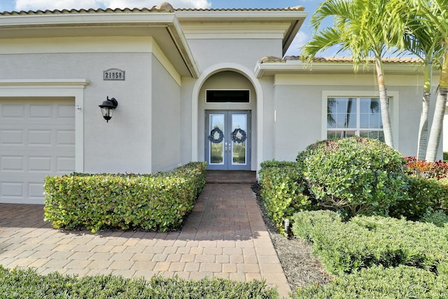 entrance to property with french doors, an attached garage, and stucco siding