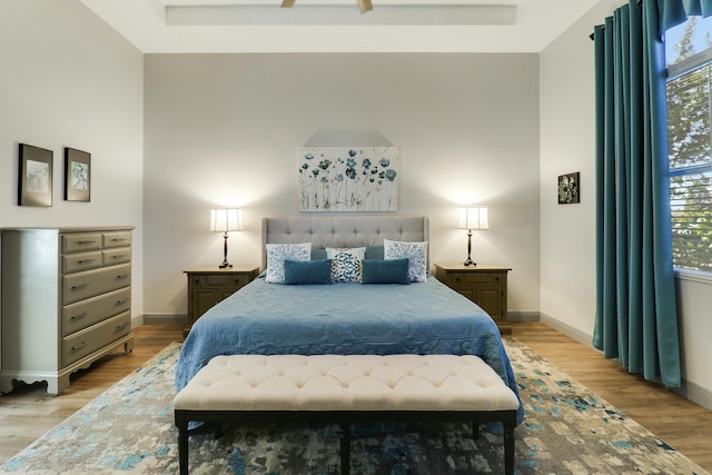 bedroom with a towering ceiling, a raised ceiling, baseboards, and wood finished floors