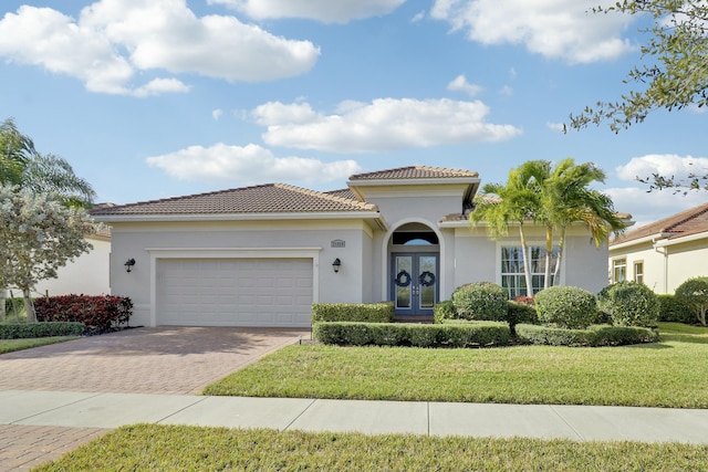 mediterranean / spanish-style home with stucco siding, decorative driveway, french doors, a front yard, and a garage