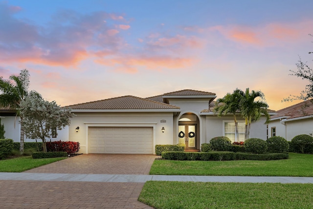 view of front of house featuring stucco siding, french doors, decorative driveway, a yard, and a garage