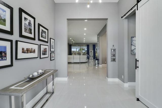 corridor featuring a barn door, light tile patterned flooring, recessed lighting, and baseboards