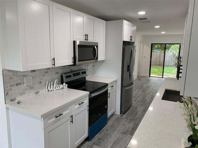 kitchen featuring white cabinets, decorative backsplash, hardwood / wood-style flooring, stainless steel appliances, and light stone countertops