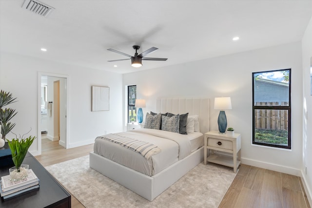 bedroom with multiple windows, ceiling fan, ensuite bathroom, and light hardwood / wood-style floors