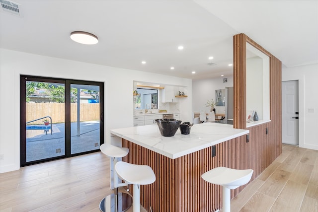 kitchen featuring white cabinets, light hardwood / wood-style floors, a breakfast bar, stainless steel fridge, and sink