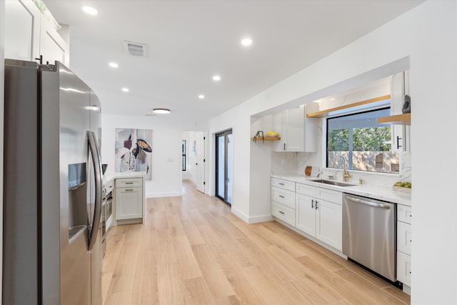 kitchen featuring appliances with stainless steel finishes, tasteful backsplash, light hardwood / wood-style floors, sink, and white cabinetry