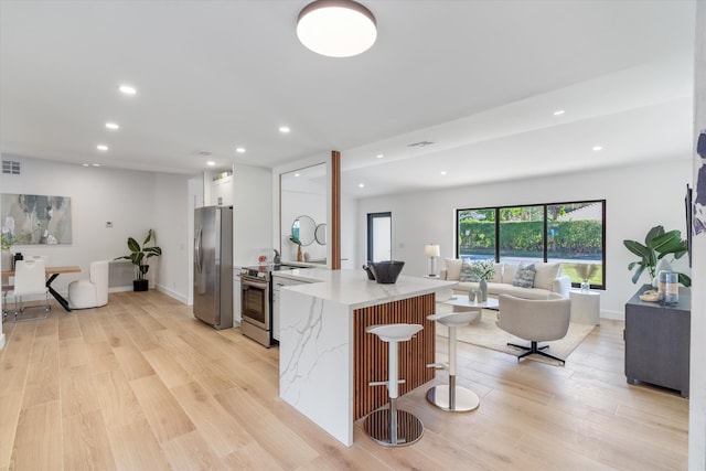 kitchen with white cabinetry, a kitchen bar, light hardwood / wood-style floors, stainless steel appliances, and light stone countertops