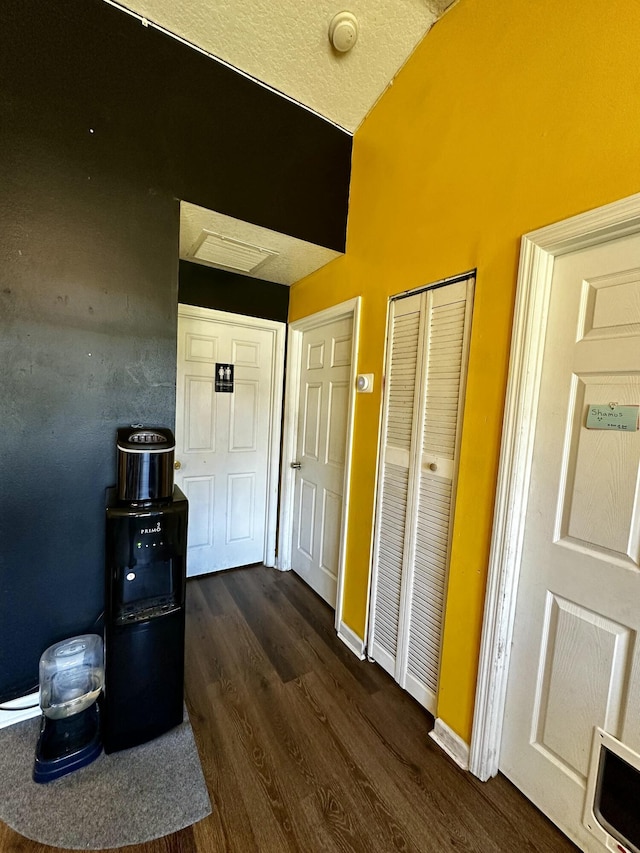 hallway featuring dark wood-type flooring, vaulted ceiling, and a textured ceiling