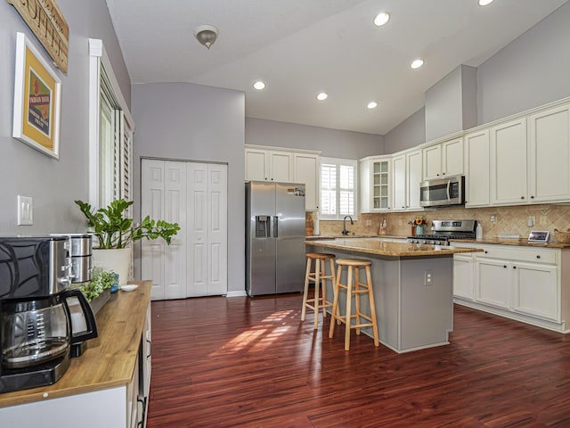 kitchen featuring a kitchen island, appliances with stainless steel finishes, dark wood-type flooring, and high vaulted ceiling