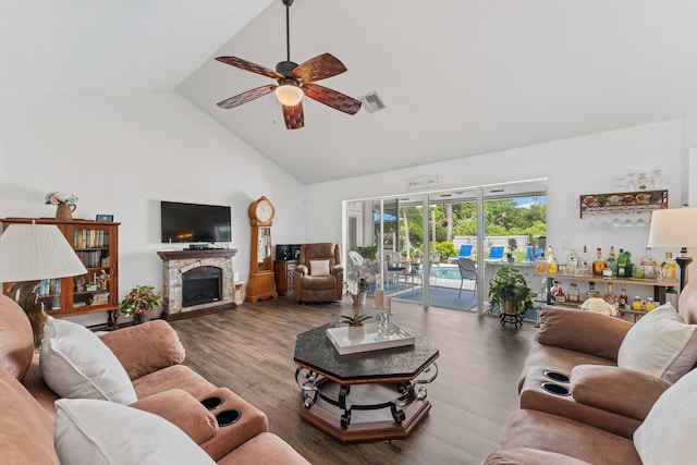 living area featuring visible vents, ceiling fan, wood finished floors, a stone fireplace, and high vaulted ceiling