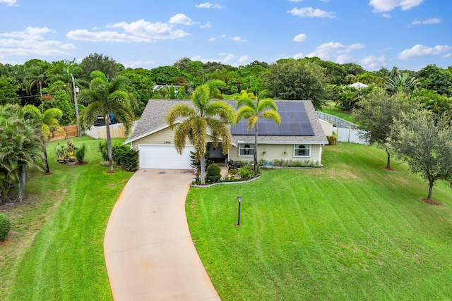 ranch-style house with a shingled roof, roof mounted solar panels, fence, driveway, and a front lawn