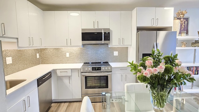 kitchen featuring tasteful backsplash, stainless steel appliances, light hardwood / wood-style flooring, and white cabinets