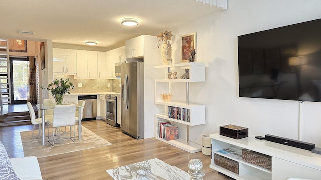 kitchen featuring white cabinetry, stainless steel appliances, light hardwood / wood-style flooring, and backsplash