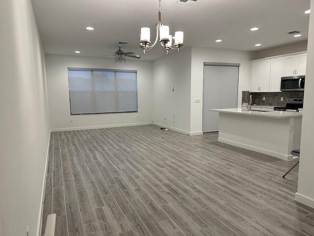 kitchen featuring electric range oven, white cabinets, decorative backsplash, hanging light fixtures, and light hardwood / wood-style floors