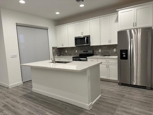 kitchen featuring a kitchen island with sink, sink, stainless steel appliances, and white cabinets