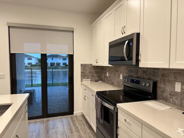 kitchen with electric stove, white cabinetry, tasteful backsplash, and light hardwood / wood-style flooring