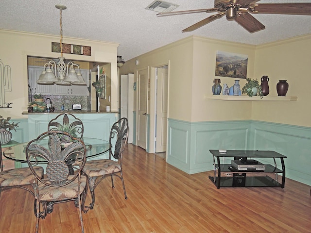 dining room with ornamental molding, ceiling fan with notable chandelier, a textured ceiling, and light wood-type flooring