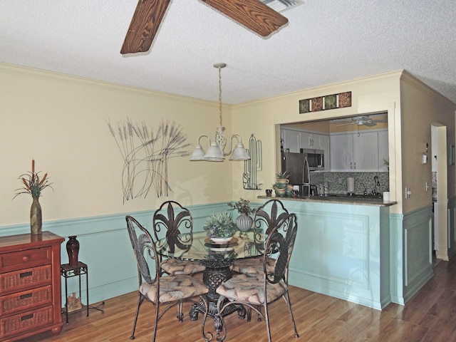 dining space featuring ceiling fan with notable chandelier, ornamental molding, dark hardwood / wood-style floors, and a textured ceiling