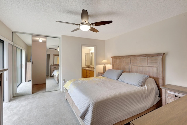 bedroom with ceiling fan, ensuite bathroom, light carpet, and a textured ceiling