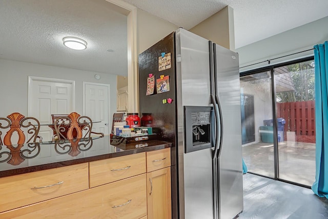 kitchen with stainless steel fridge with ice dispenser, light brown cabinetry, and a textured ceiling