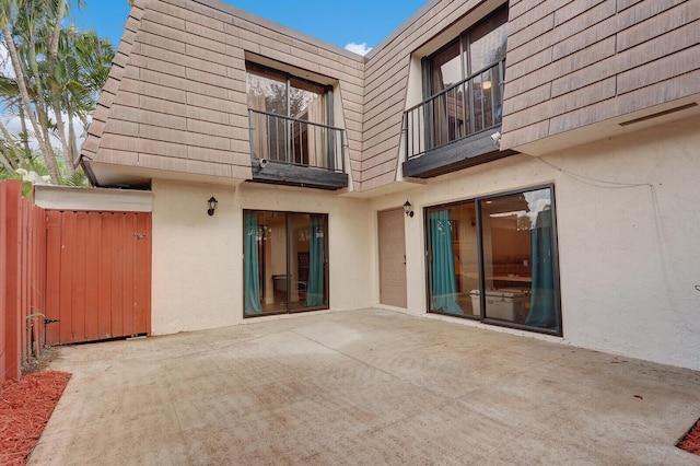 back of house with fence, stucco siding, mansard roof, a balcony, and a patio